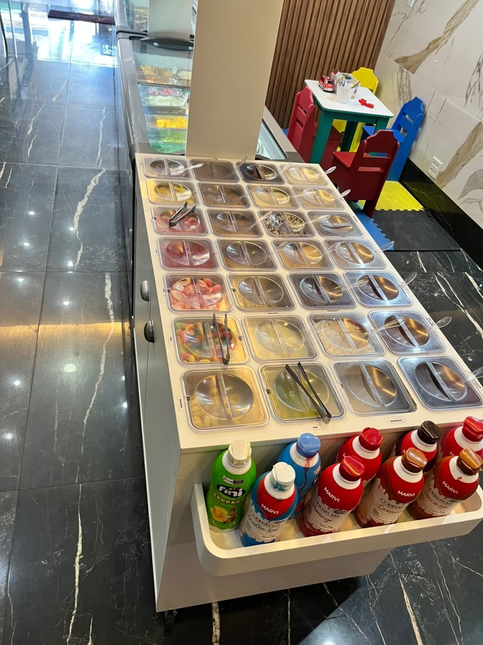 Balcão self-service com toppings, frutas e caldas para montar o açaí